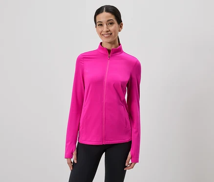 Une femme souriante portant une veste zippée rose et un legging noir sur fond gris.