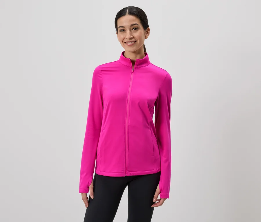 Une femme souriante portant une veste zippée rose et un legging noir sur fond gris.