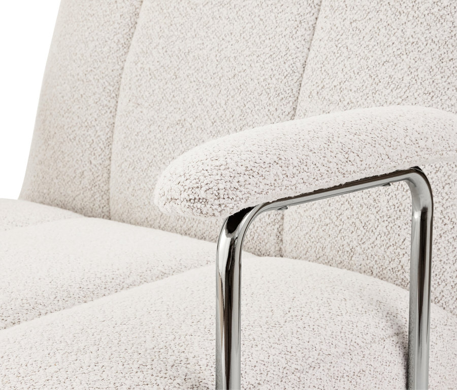 Gros plan d'un fauteuil avec accoudoir et revêtement bouclé blanc sur un cadre métallique chromé.