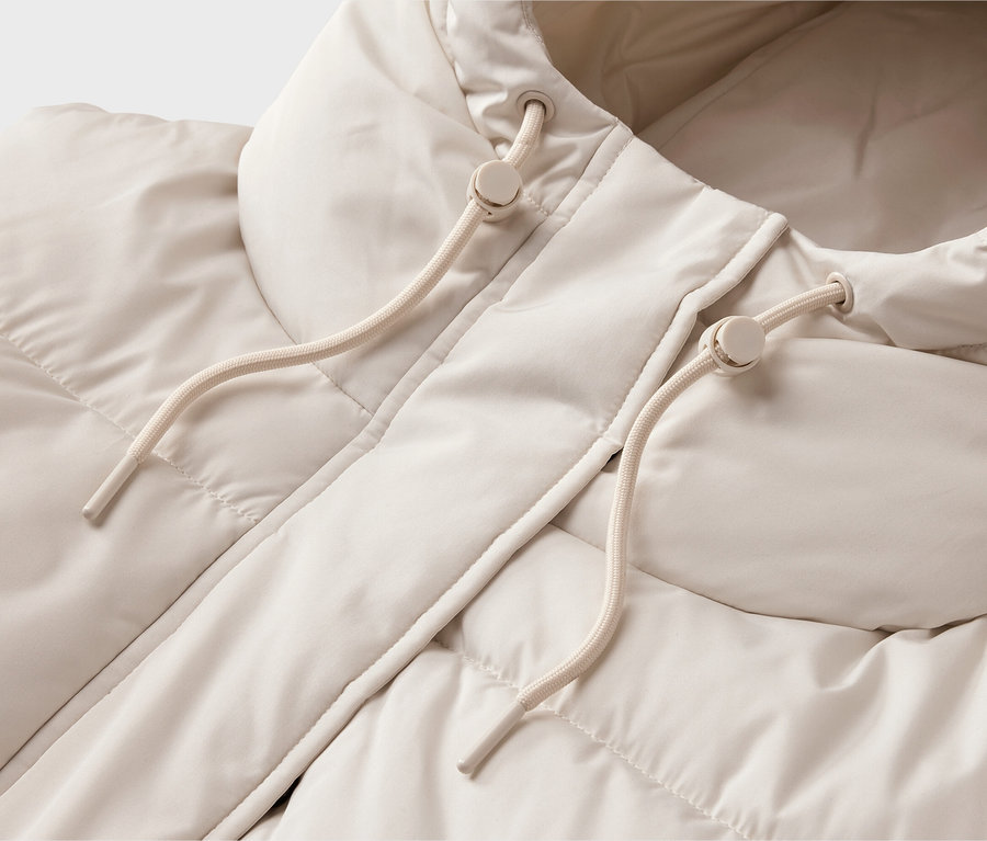 Gros plan d'une doudoune beige clair avec capuche. La veste a une texture matelassée et la capuche est dotée de deux cordons de serrage crème avec des stoppeurs en plastique.