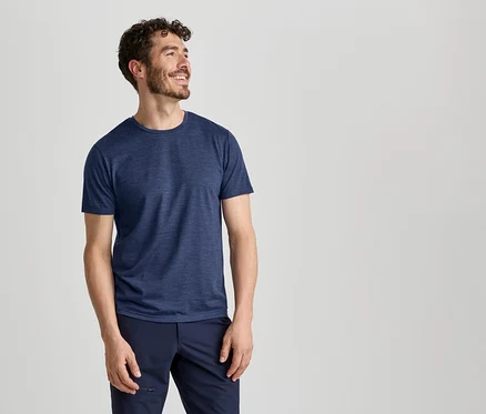 Un homme portant un t-shirt bleu et un pantalon bleu foncé sourit et regarde vers la droite.