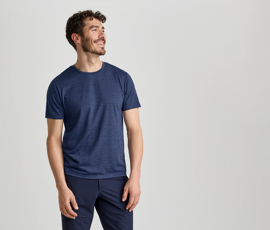 Un homme portant un t-shirt bleu et un pantalon bleu foncé sourit et regarde vers la droite.