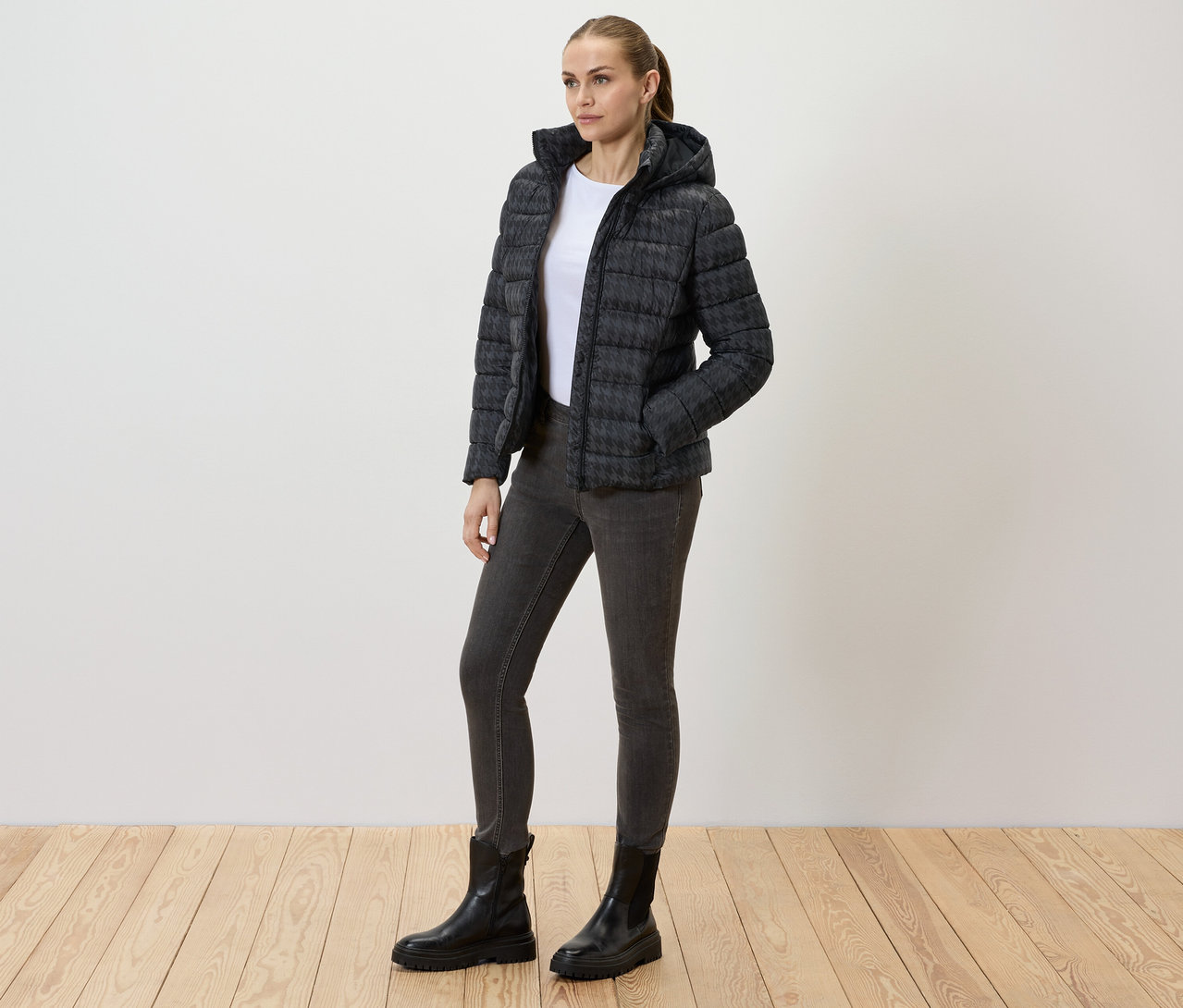 Femme portant une veste matelassée imprimée avec capuche, un jean et des bottes noires.