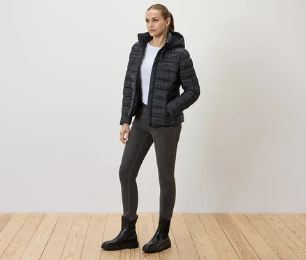 Femme portant une veste matelassée imprimée avec capuche, un jean et des bottes noires.