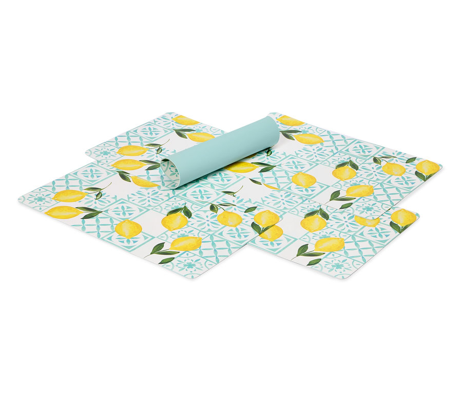Sur un fond blanc, des sets de table à motif citron et un tapis bleu clair enroulé.