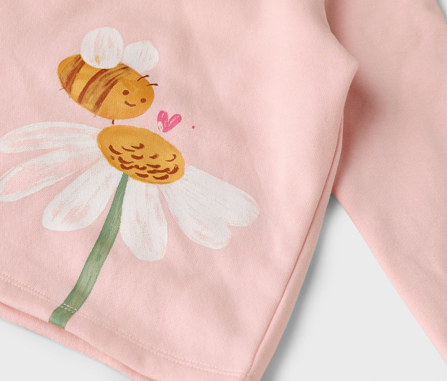 Sur un tissu rose, une abeille peinte sur une fleur de marguerite.