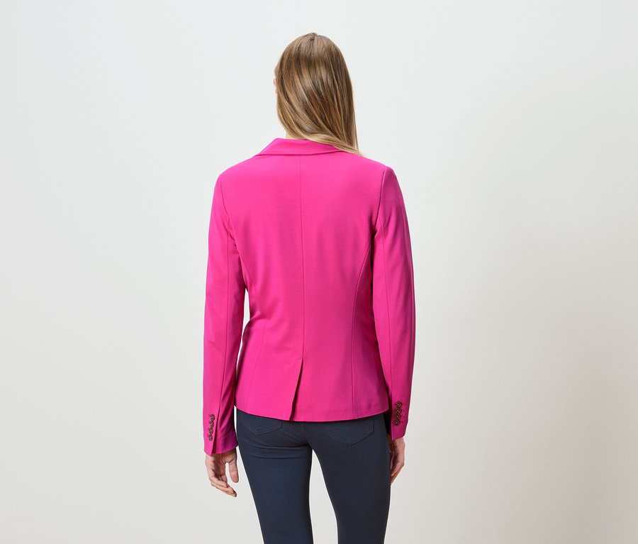 Vue de dos d'une femme aux longs cheveux blonds portant un blazer rose et un jean foncé.