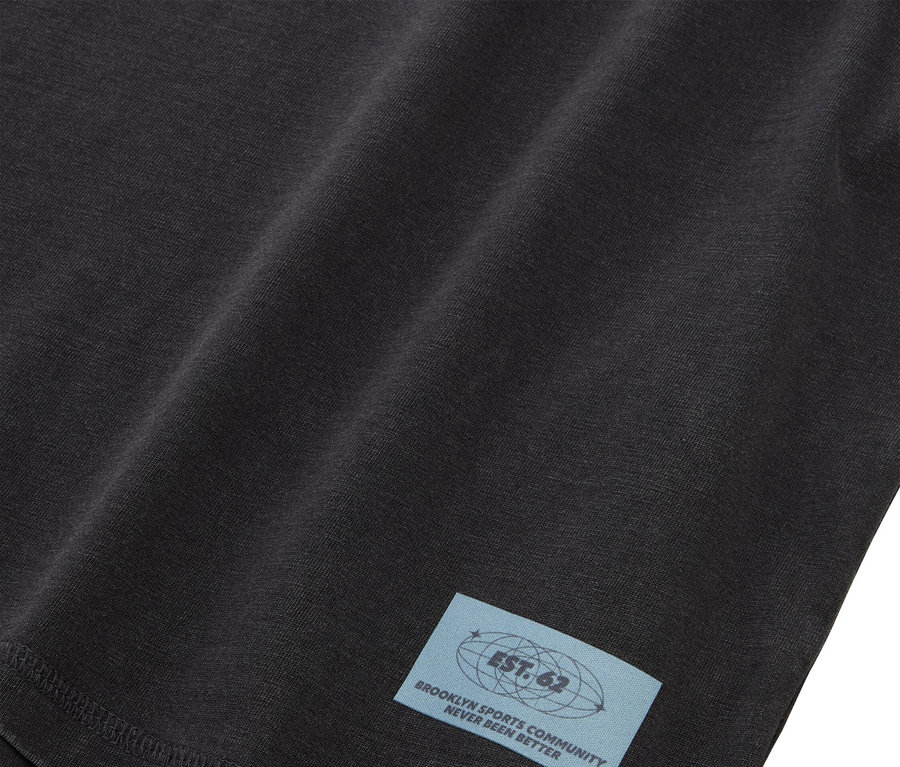 Gros plan sur un tissu noir avec une étiquette bleu clair portant l'inscription "EST. 62 BROOKLYN SPORTS COMMUNITY NEVER BEEN BETTER".