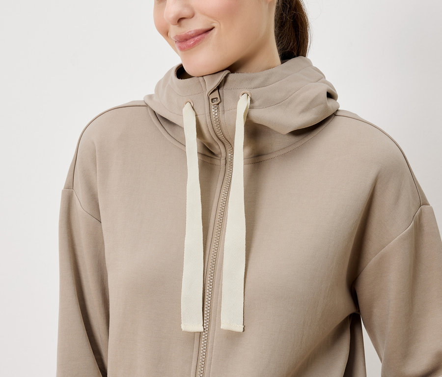 Une femme porte un sweat à capuche beige zippé.