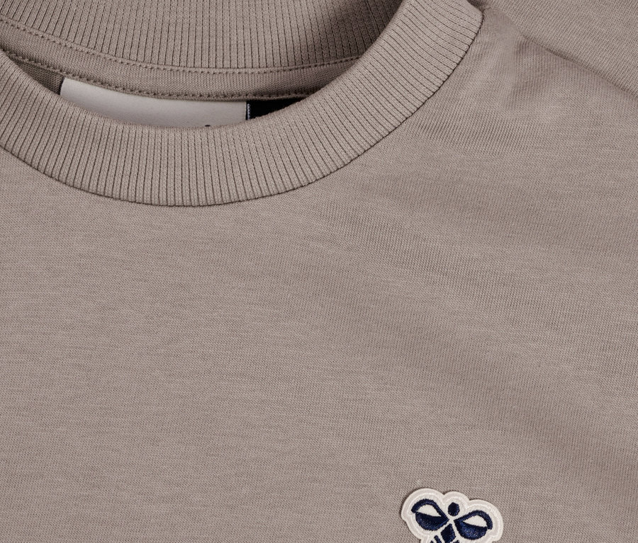 Gros plan d'un t-shirt gris avec un petit logo brodé.