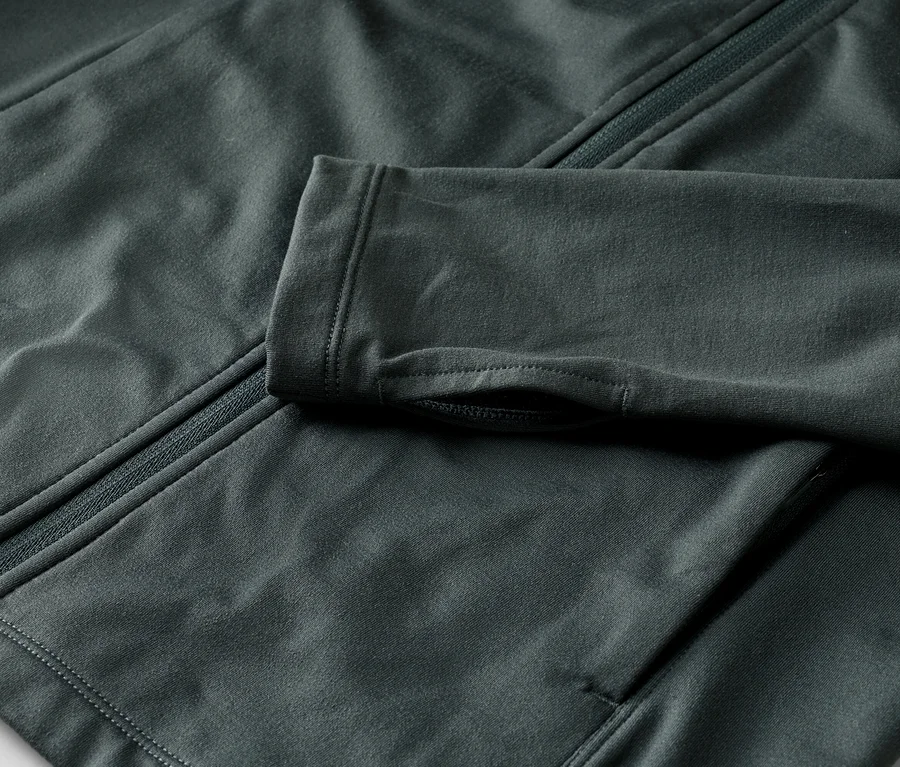 Gros plan d'une veste gris foncé avec fermeture éclair et trous pour les pouces sur la manche.