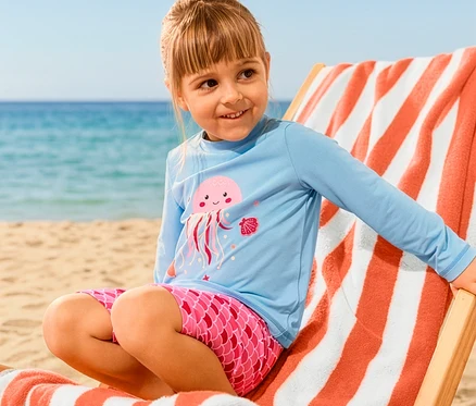 Une fille assise sur une chaise longue avec un linge de bain XL porte un ensemble pour enfant avec indice de protection UV 50+, méduse.