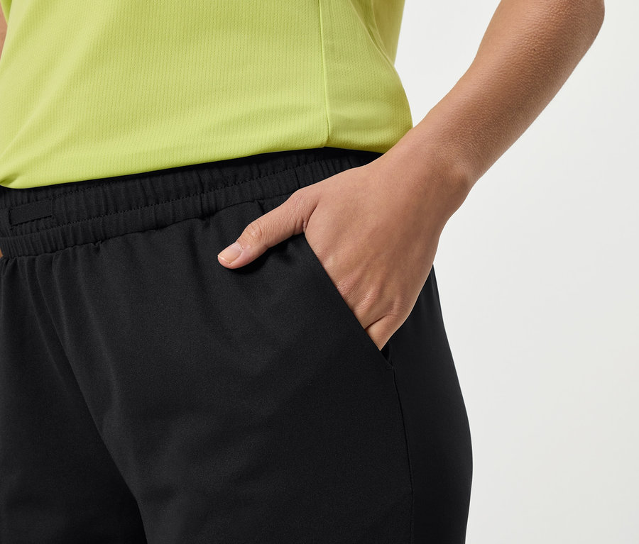 Gros plan d'une personne portant un pantalon de survêtement noir et un haut jaune, la main dans sa poche.