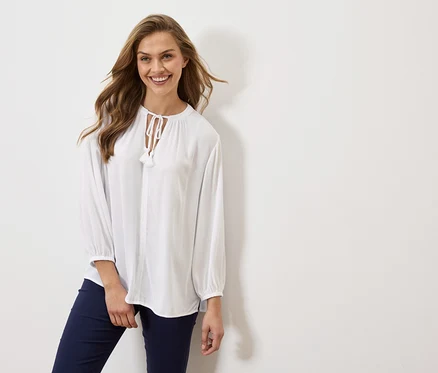 Femme portant un chemisier blanc à manches longues et un pantalon bleu marine.