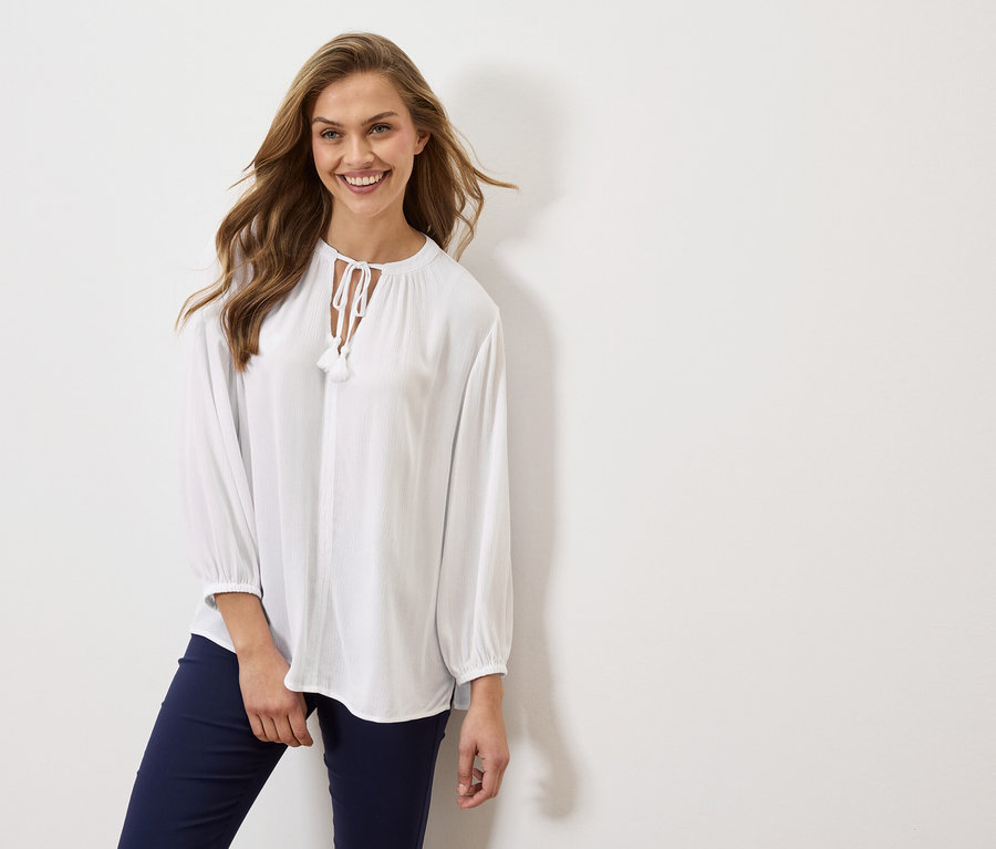 Femme portant un chemisier blanc à manches longues et un pantalon bleu marine.