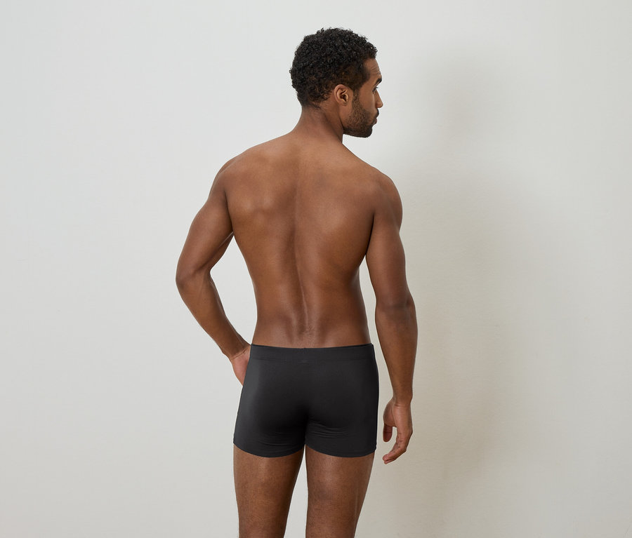 Un homme afro-américain vu de dos, torse nu et portant des sous-vêtements noirs, sur un fond clair.