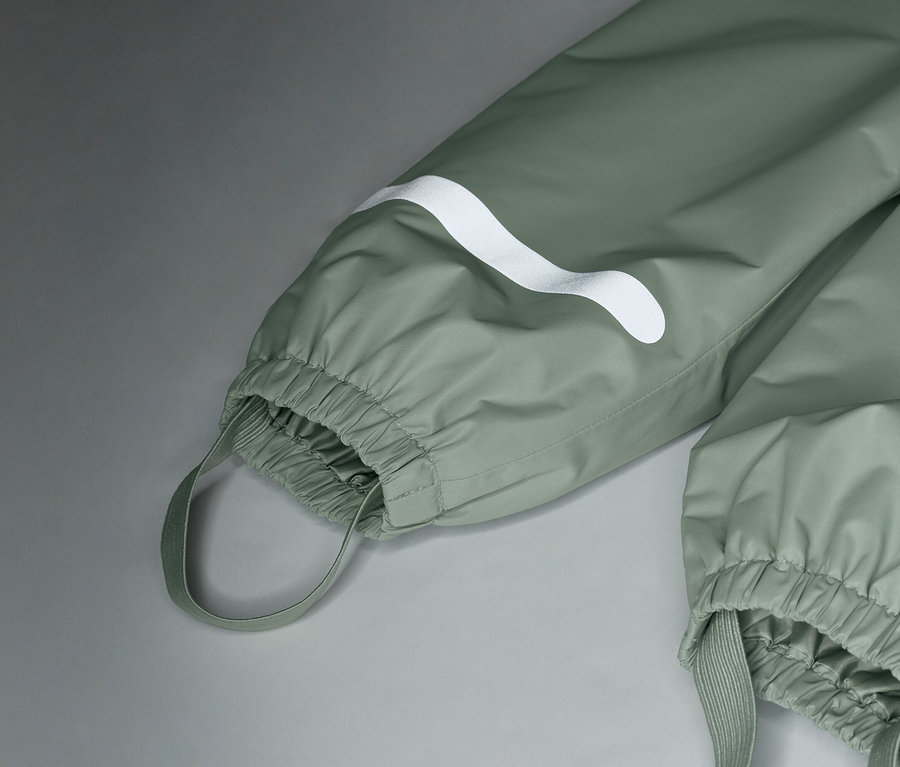 Gros plan sur un pantalon de pluie vert clair avec un logo blanc et des poignets élastiques.