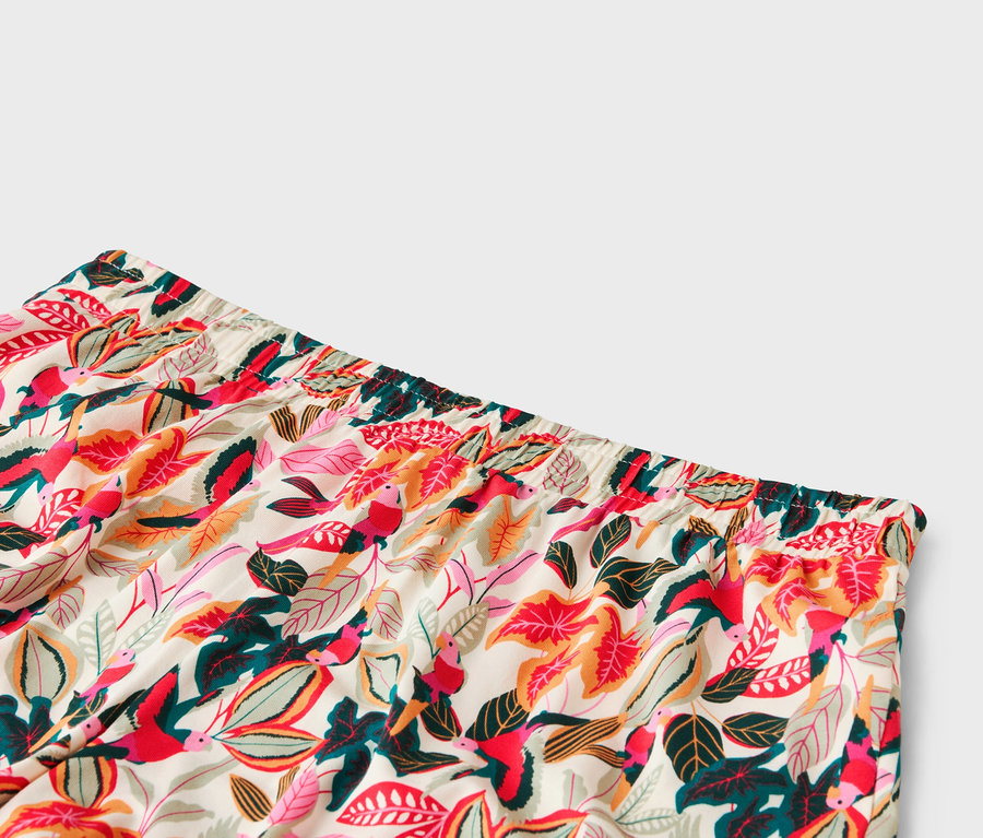 Gros plan sur la ceinture d'un pantalon avec un motif de feuilles et d'oiseaux dans les tons rouge, rose, vert et orange.