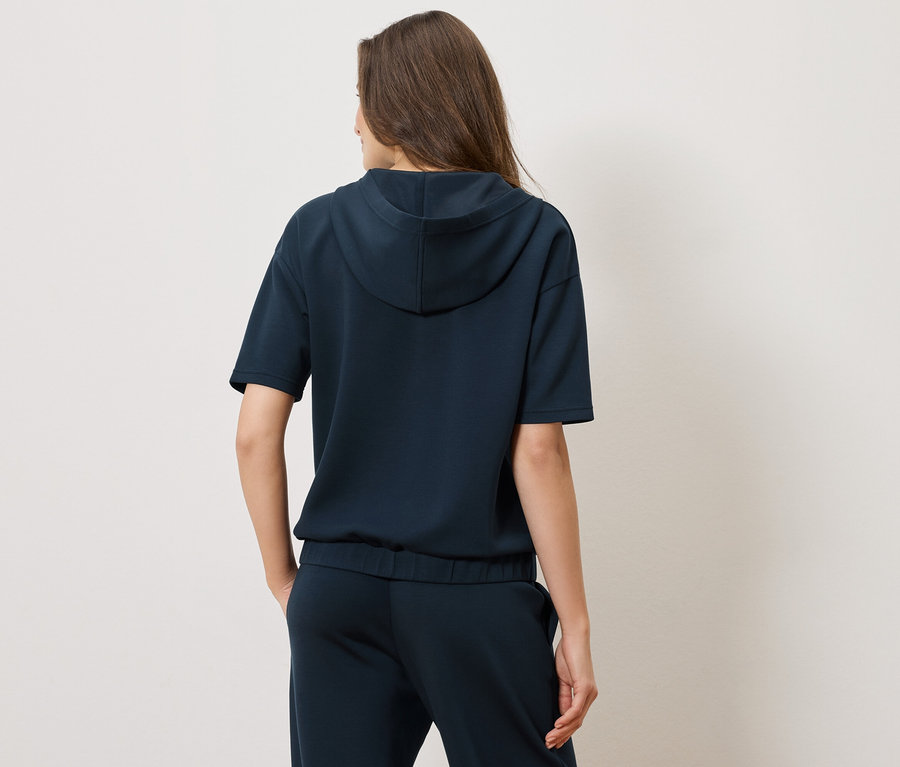 Vue arrière d'une femme portant un sweat à capuche bleu marine à manches courtes et un pantalon assorti.