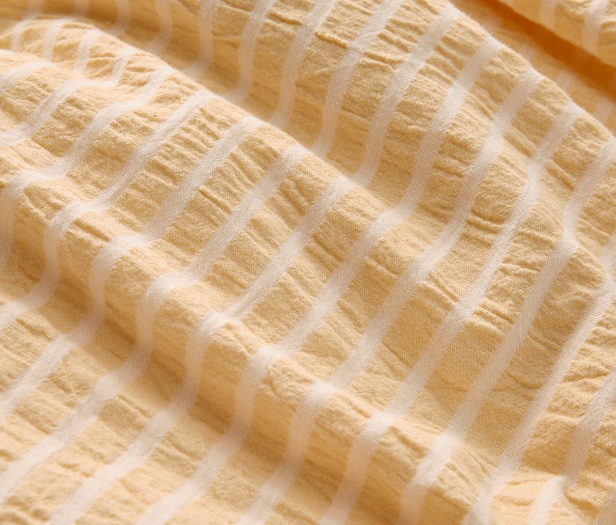 Gros plan d'un tissu froissé jaune clair avec des rayures blanches.