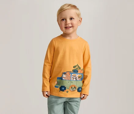Un garçon souriant aux cheveux blonds porte un t-shirt orange à manches longues avec un imprimé de voiture verte.
