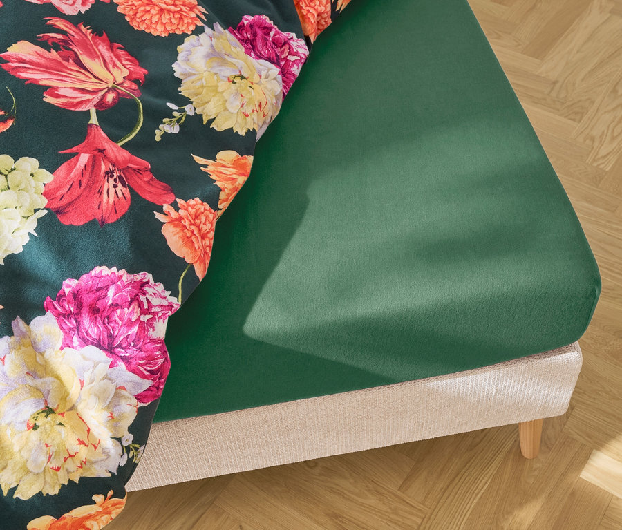 Lit avec drap-housse vert foncé et linge de lit vert foncé à motifs floraux.