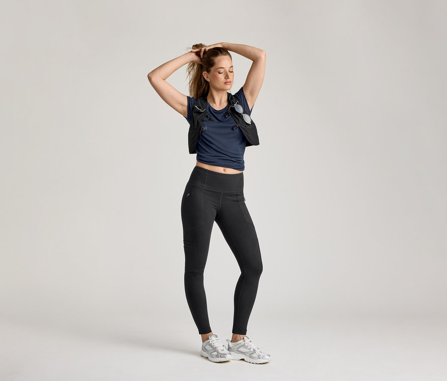 Femme posant en leggings d’extérieur, t-shirt bleu marine et gilet sur fond clair.