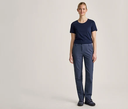 Une jeune femme se tient de face devant un fond clair, vêtue d'un t-shirt bleu marine, d'un pantalon bleu et de chaussures bleu foncé.