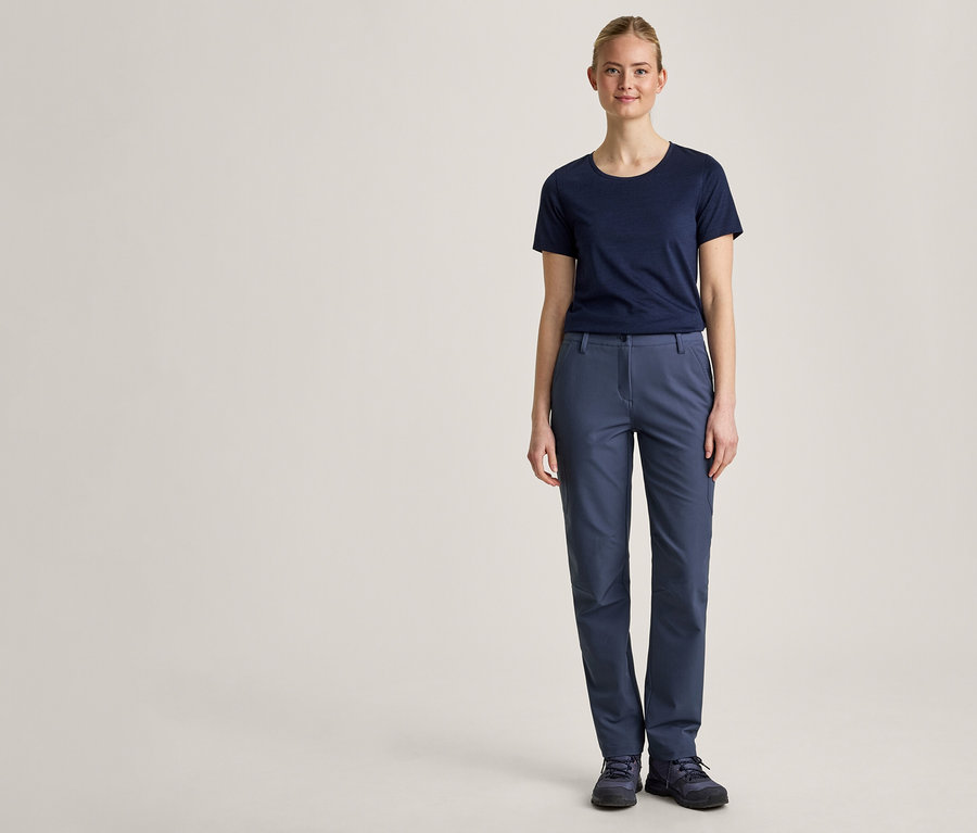 Une jeune femme se tient de face devant un fond clair, vêtue d'un t-shirt bleu marine, d'un pantalon bleu et de chaussures bleu foncé.
