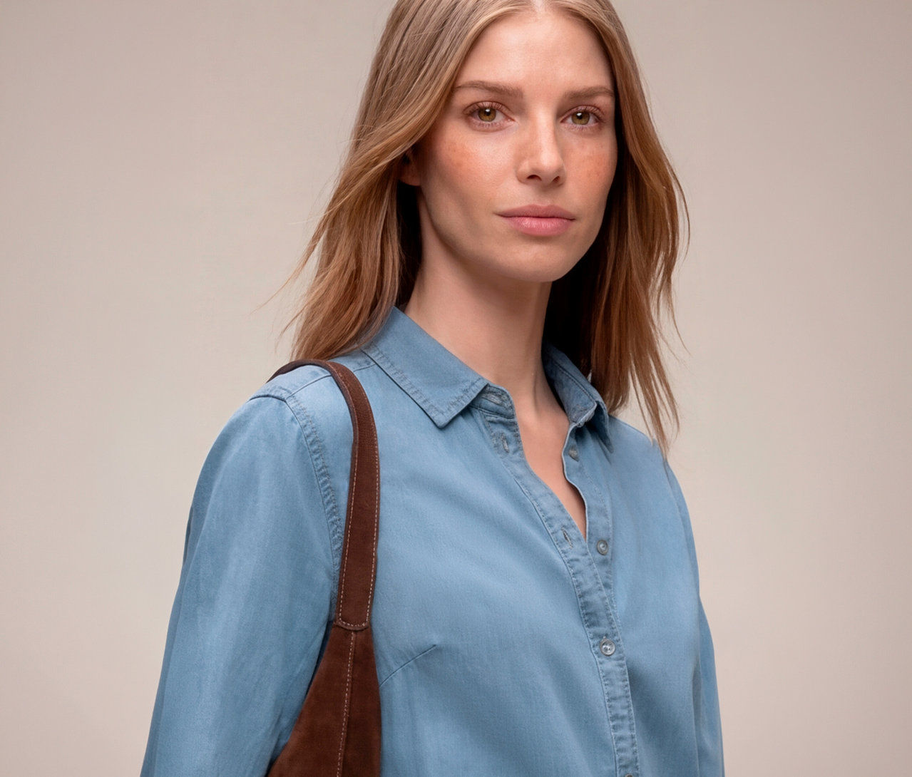 Femme aux cheveux châtain clair portant une chemise en jean bleu clair, avec un sac marron à l'épaule.