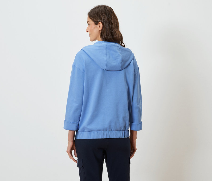 Femme portant un sweat à capuche bleu clair et un pantalon bleu marine, vue de dos.