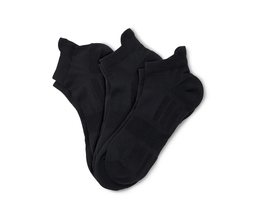 Trois chaussettes de cheville noires sont soigneusement pliées et disposées sur un fond blanc.