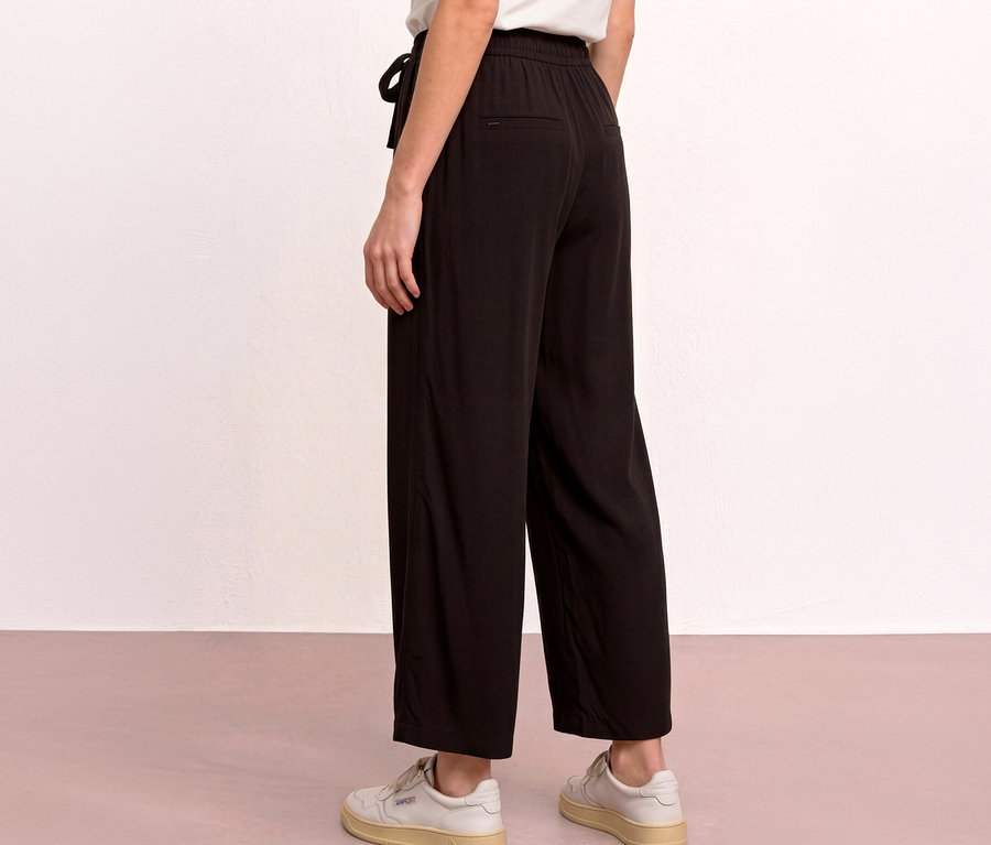 Une personne est debout, dos à l'appareil photo, portant un culotte 7/8 Street One « EMMA » noire avec un cordon de serrage et des baskets blanches.
