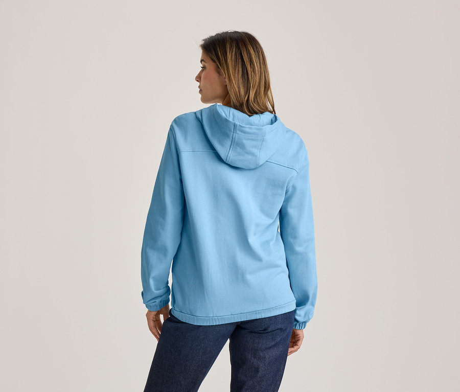 Femme de dos portant un sweat à capuche bleu clair et un jean foncé, regardant vers la droite.