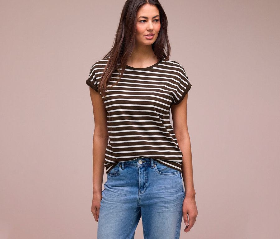 Femme aux longs cheveux foncés portant un t-shirt Street One rayé marron foncé et blanc et un jean bleu clair, regardant à droite.