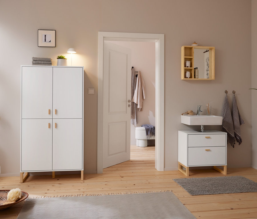 Salle de bain lumineuse avec parquet en bois et murs gris clair. À gauche, une armoire blanche avec une lampe de table à LED sans fil blanche et une plante. À droite, un miroir avec étagères est suspendu au-dessus d'un lavabo avec meuble sous-vasque. Une porte ouverte mène à une pièce adjacente.