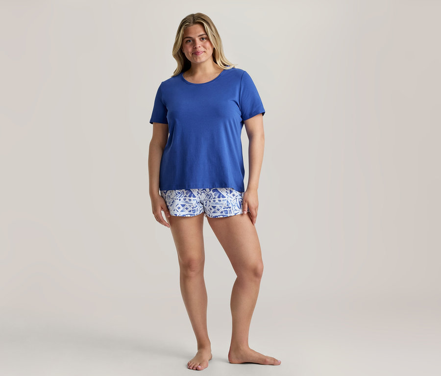Femme souriante portant un t-shirt bleu roi et un short à motifs d'un ensemble pyjama shorty.