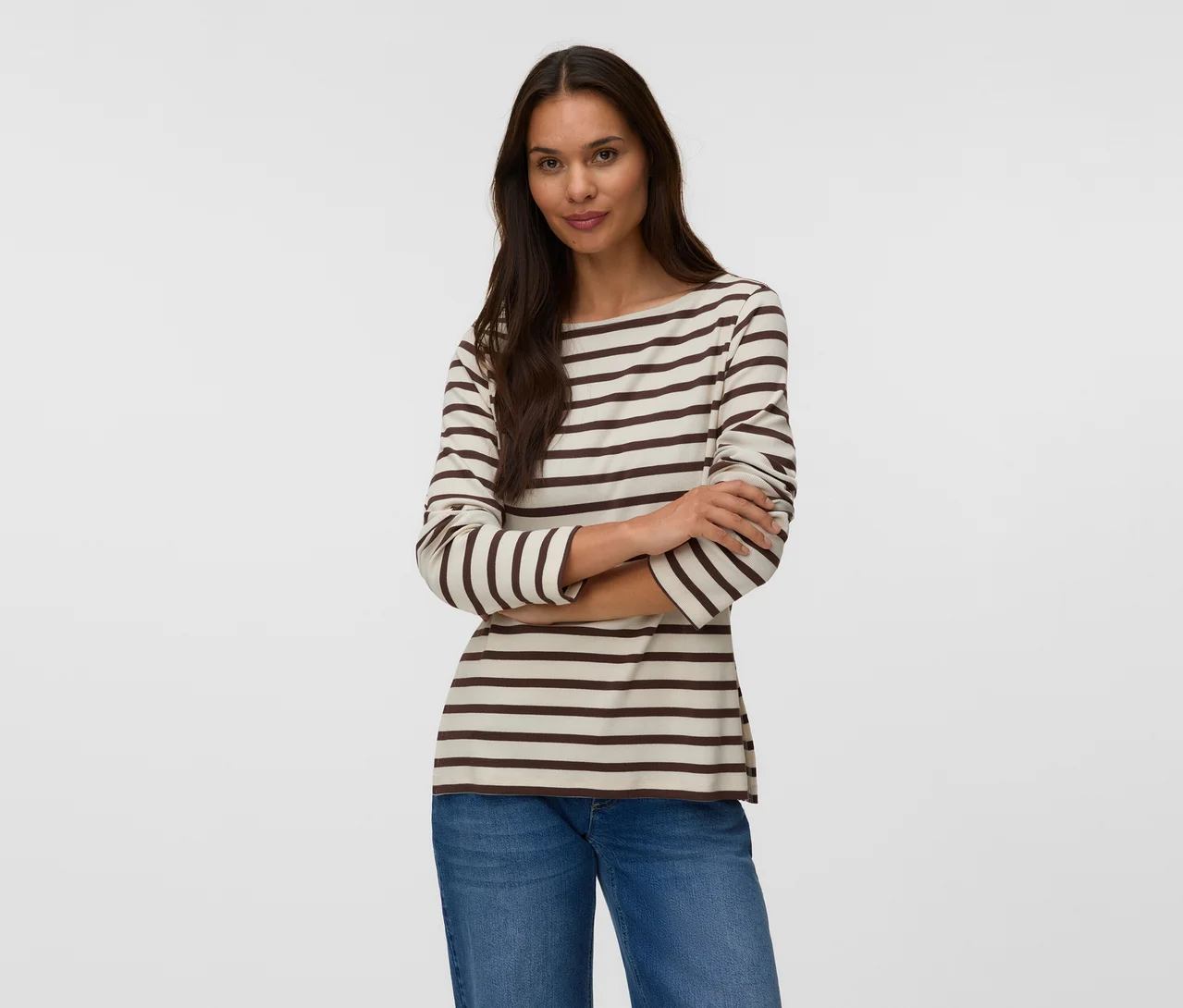 Femme aux bras croisés, portant un t-shirt rayé crème et marron et un jean bleu.