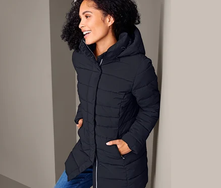 Une femme souriante pose dans un manteau matelassé.