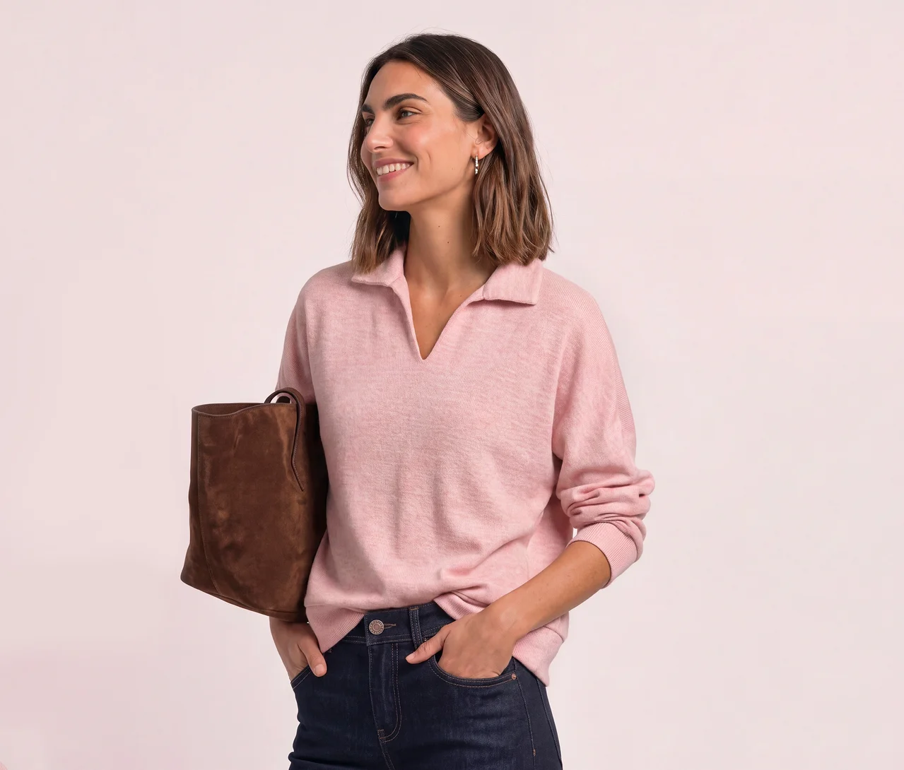 Femme souriante aux cheveux courts, portant un polo Street One rose, un jean foncé et un sac marron.