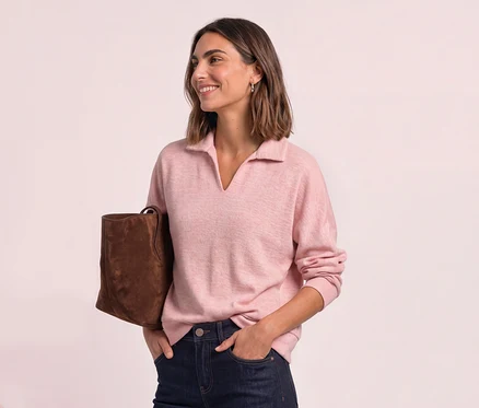 Femme souriante aux cheveux courts, portant un polo Street One rose, un jean foncé et un sac marron.
