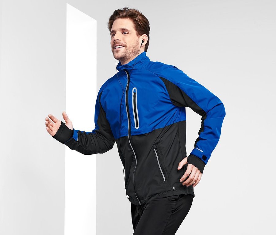 Un homme court vêtu d'une veste de sport coupe-vent bleue et noire.