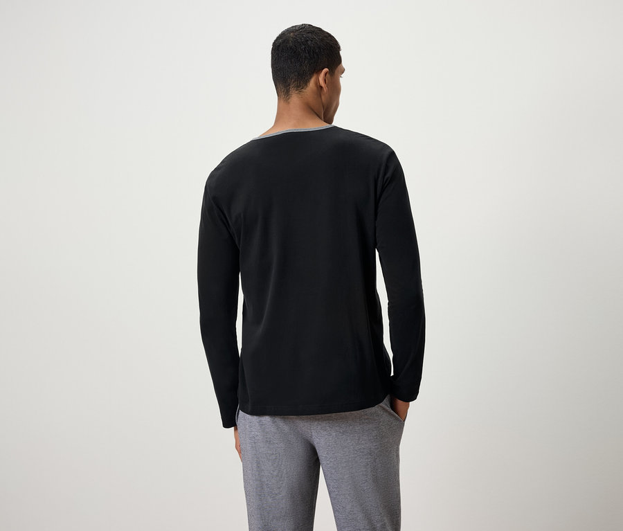 Un homme, vu de dos, porte un t-shirt noir à manches longues et un pantalon de survêtement gris.