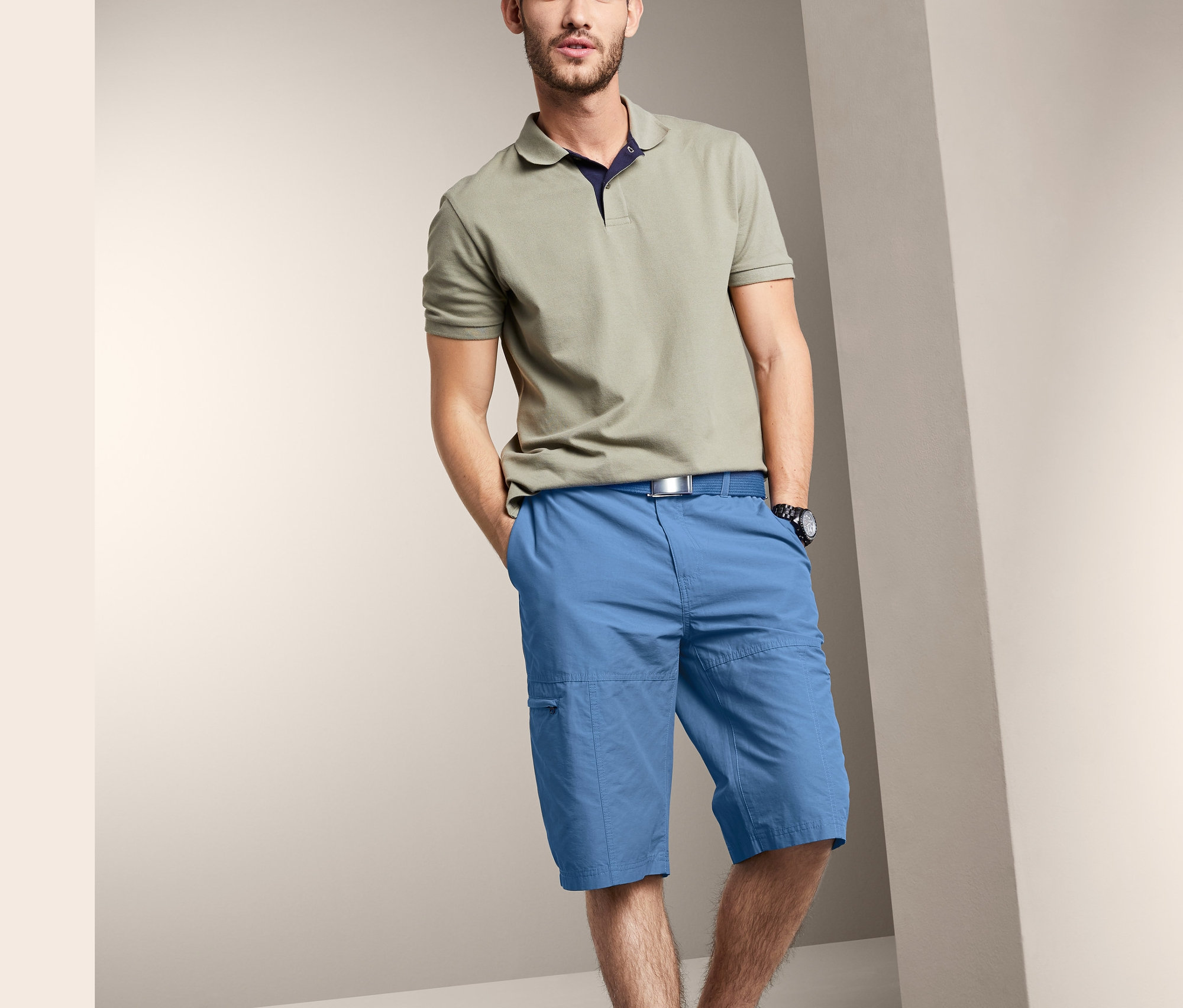 Homme posant en polo beige et bermuda bleu.
