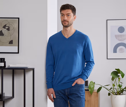 Un homme, la main dans la poche, porte un pull en lin bleu roi.