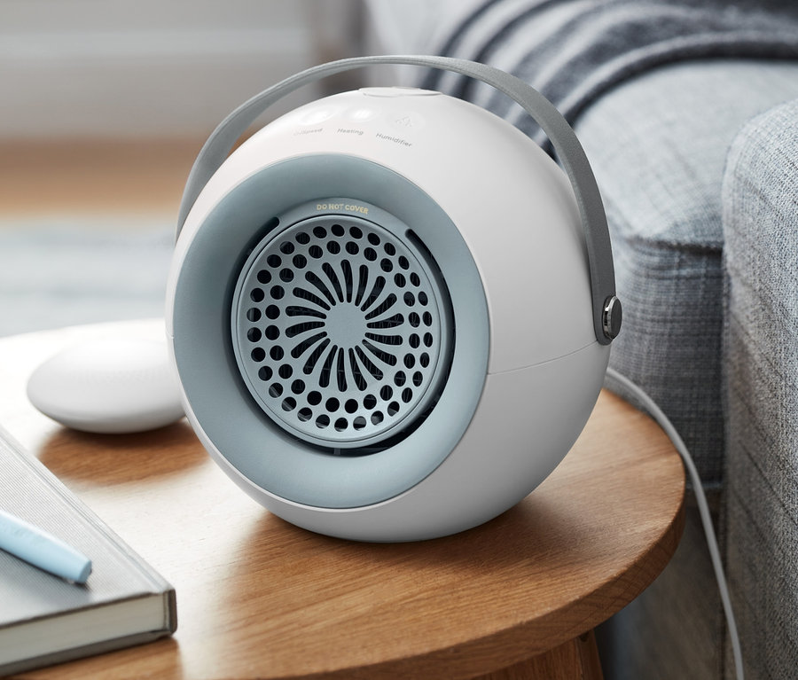 Un radiateur soufflant avec chauffe-mains amovible est posé sur une table en bois à côté d'un canapé gris.