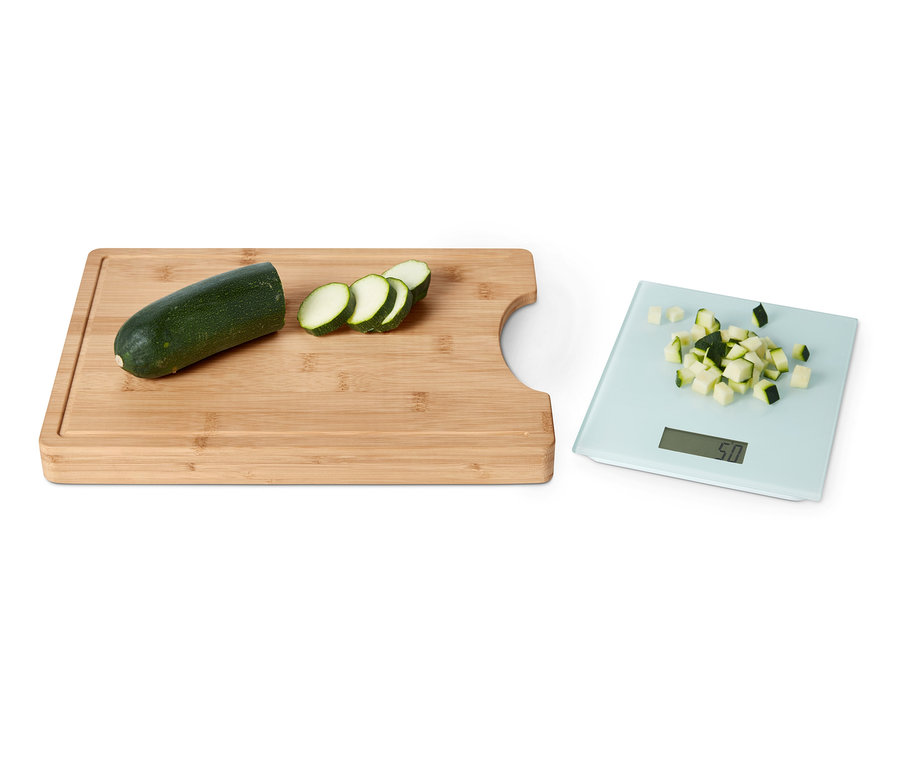 Une courgette verte, coupée en tranches, repose sur une planche à découper avec balance de cuisine amovible. Des courgettes coupées sont également présentes sur la balance.