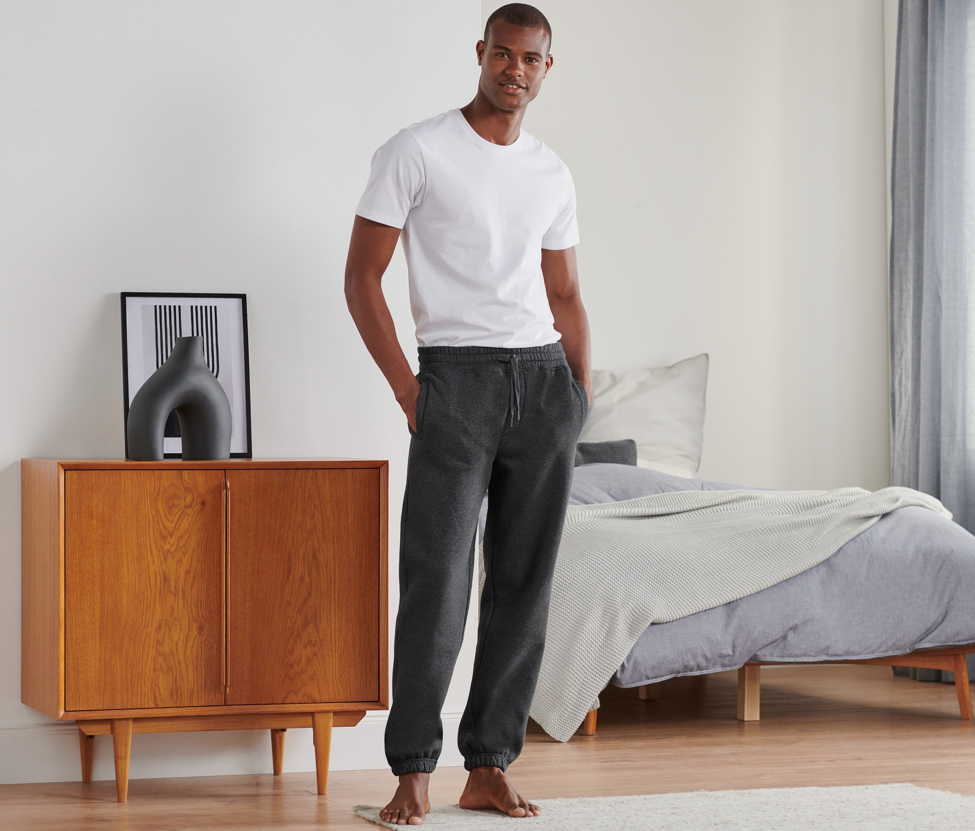 Un homme debout dans une chambre porte un pantalon de survêtement.