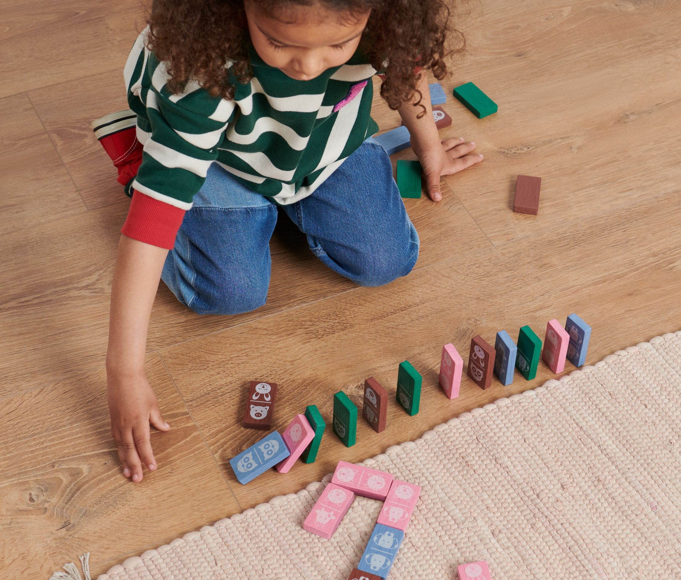 Un enfant joue par terre avec un set de dominos animaux.