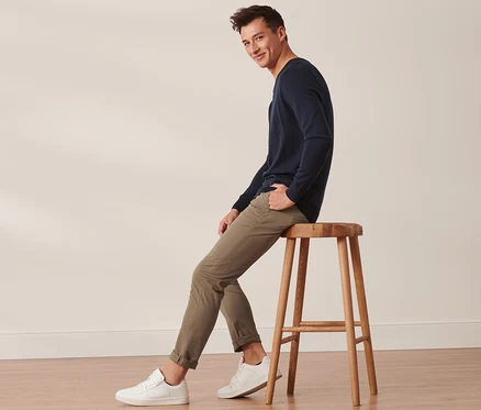 Un homme est assis sur un tabouret en bois et porte un pantalon chino sable.